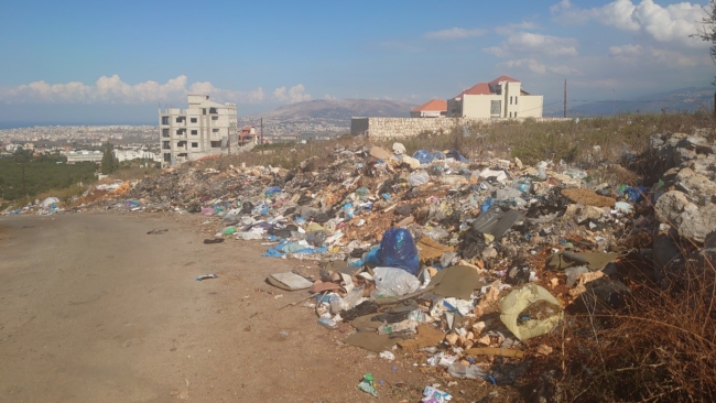 Afval wordt gedumpt en verbrand aan een doorgaande weg in Koura met in de verte op de achtergrond de contouren van de stad Tripoli. Foto genomen door auteur